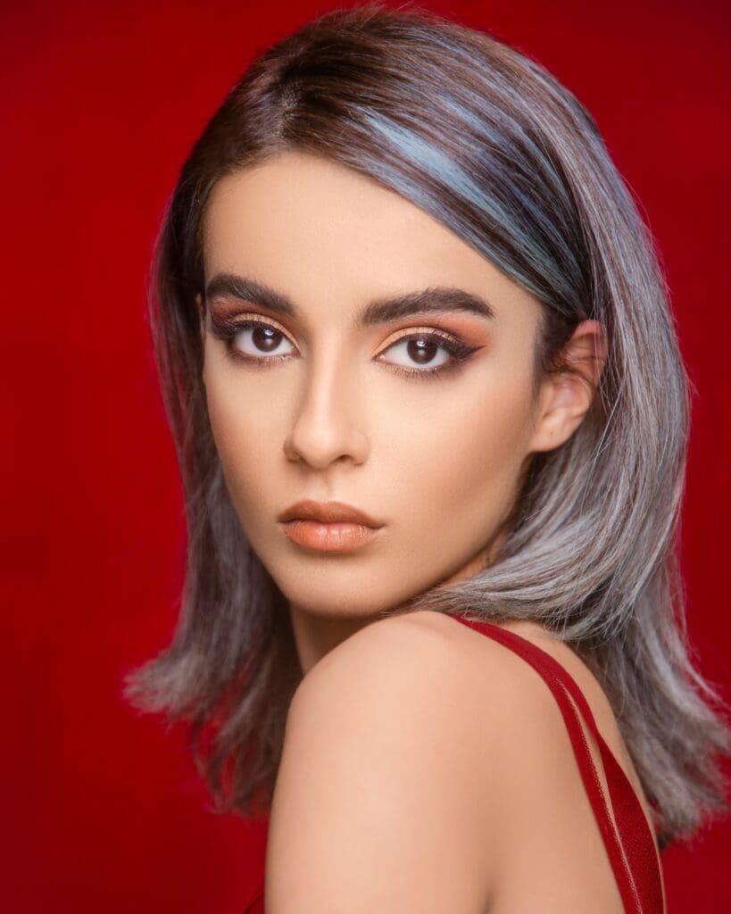 Portrait of a stylish woman with dyed hair against a vivid red background.