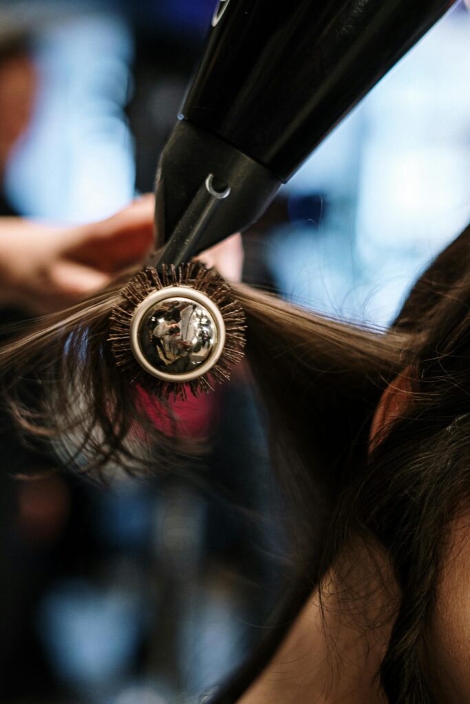 pexels-photo-3993467-3993467 Close-up of a hairstylist styling hair with a brush and dryer in a salon setting.