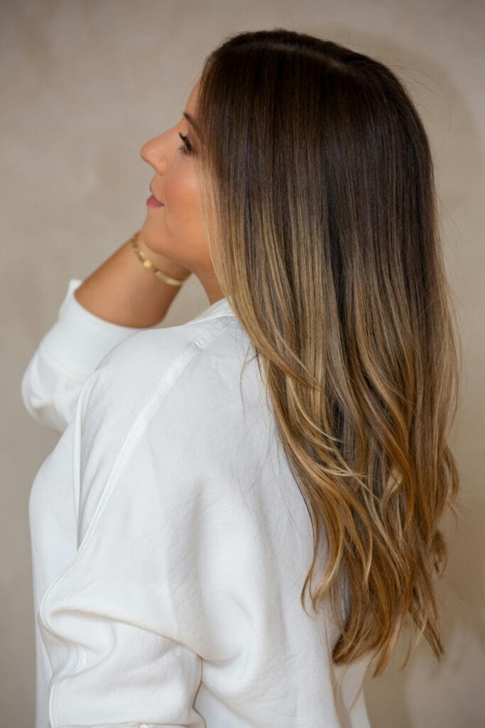 Stylish side view portrait of a woman with long brunette hair wearing a white shirt.