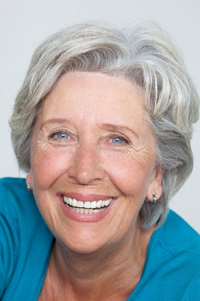 Close-up portrait of a smiling senior woman with grey hair in a studio setting.