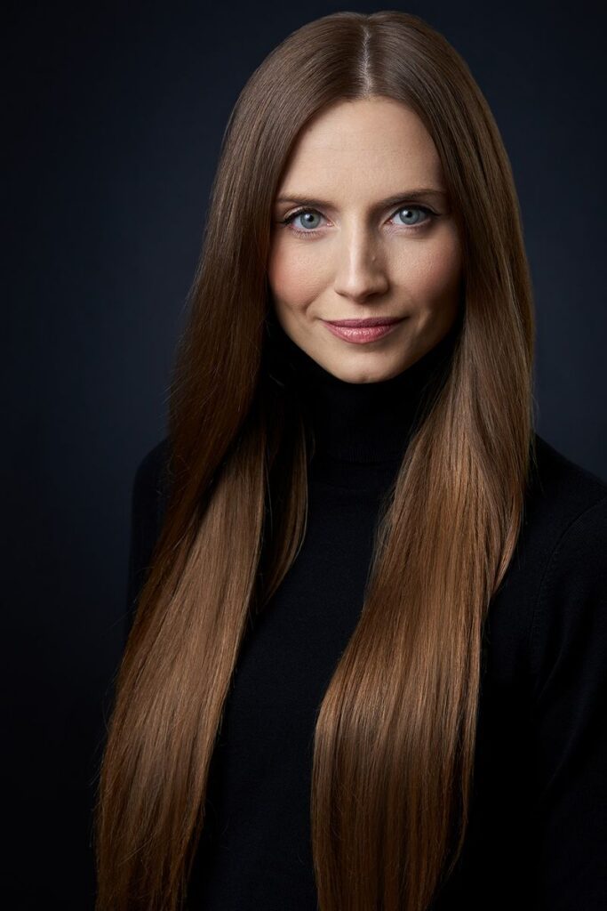 Studio portrait of a brunette woman with long hair in black outfit.
