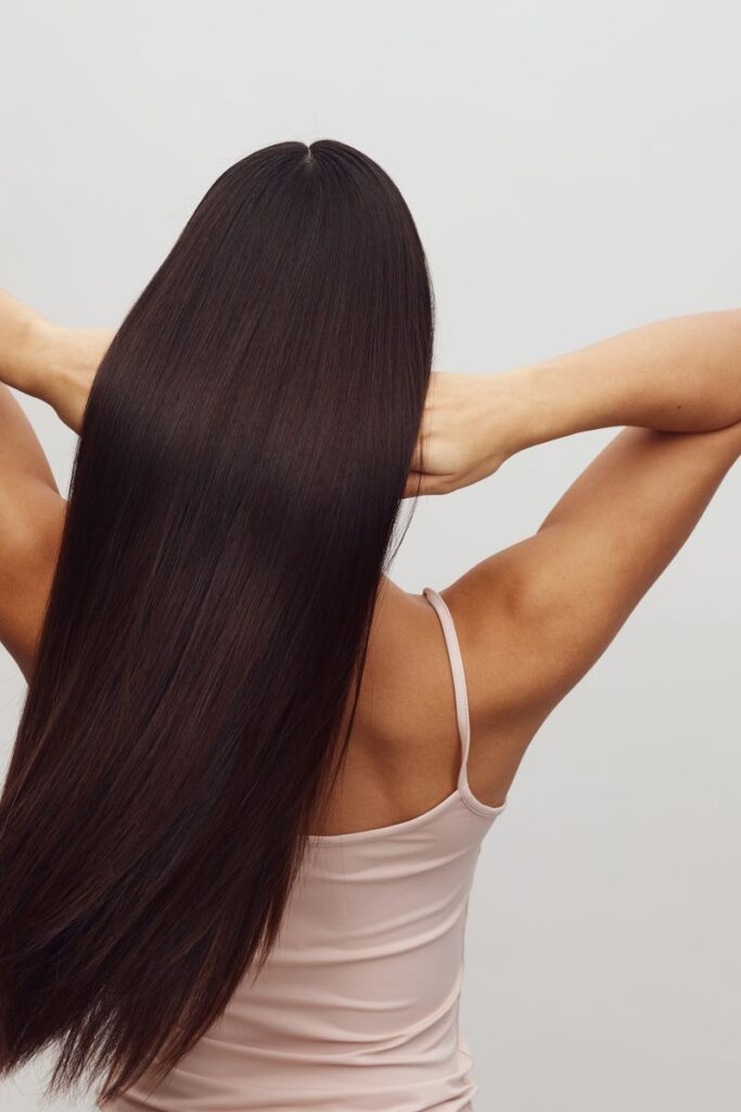 Asian woman with long, straight hair shown from behind, embracing hair care and beauty.