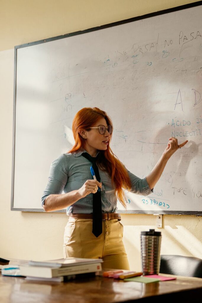 pexels-photo-37795366-37795366 A woman teacher explaining concepts on a whiteboard in a classroom setting.