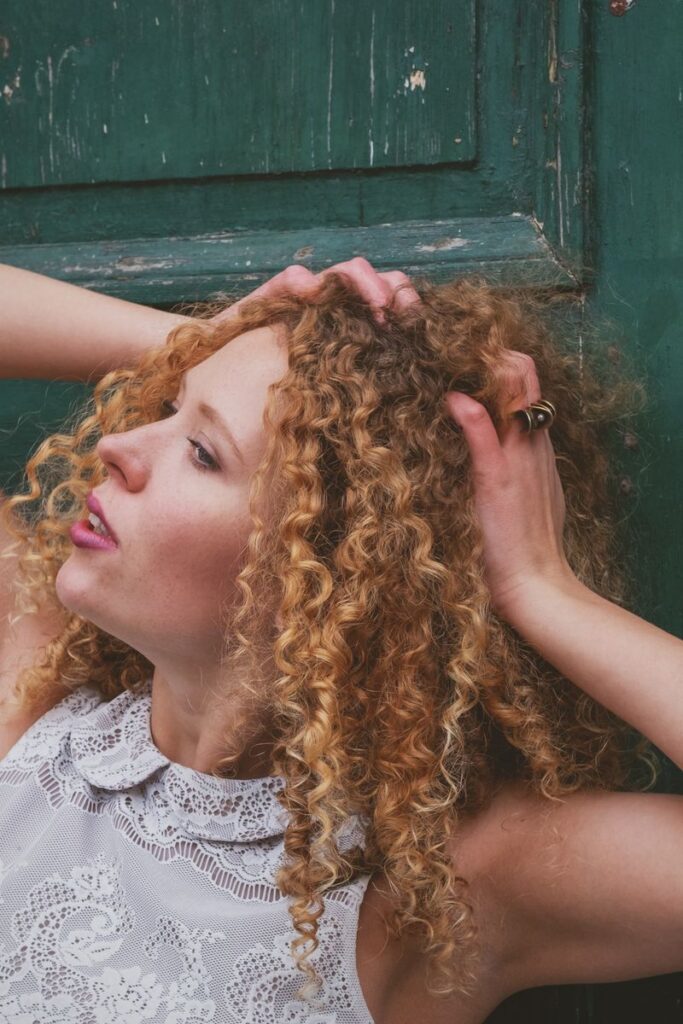 pexels-photo-37816433-37816433 Captivating outdoor portrait of a woman with curly hair against a rustic green door backdrop.