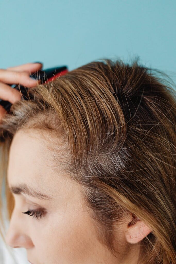 pexels-photo-7320790-7320790 Close-up of a woman brushing her hair against a blue background in a studio setting.