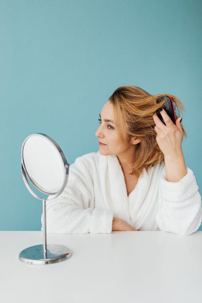 Woman in bathrobe combing hair in front of mirror, blue background.