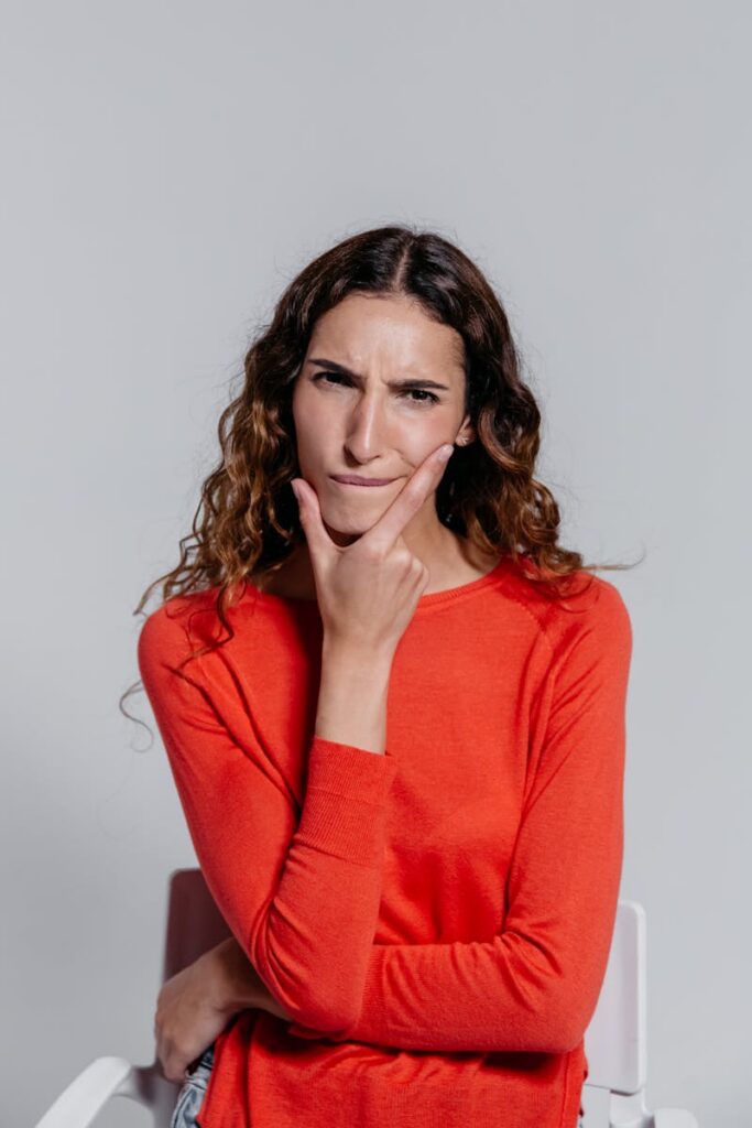 A woman in a red sweater with a thoughtful expression poses indoors, reflecting and pondering deeply.