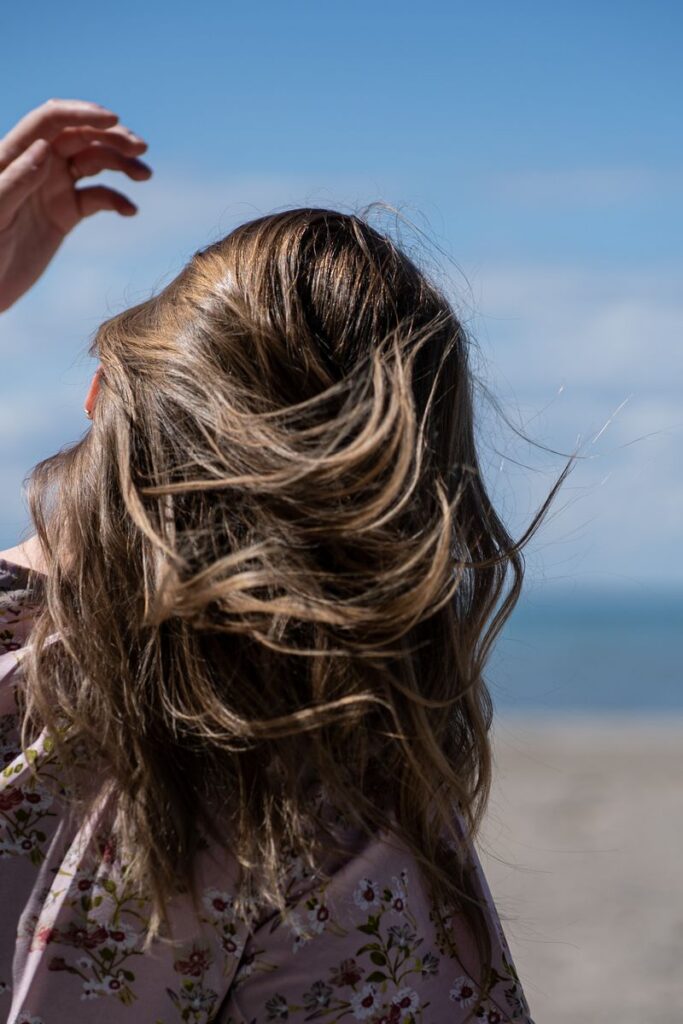 Back view of a woman with blonde hair in a floral top at a sunny beach.