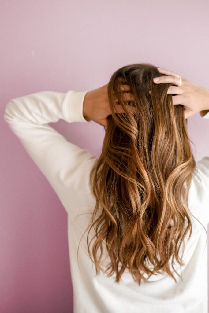pexels-photo-973401-973401 Back view of a woman with elegant long brown hair against a pink wall, showcasing stylish hair design.